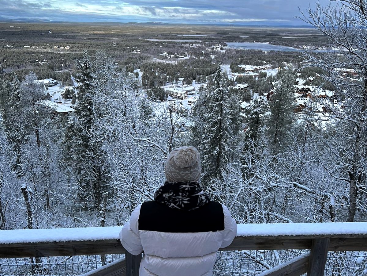 Person enjoying a snowy forest view from a scenic lookout in Levi, Finnish Lapland.